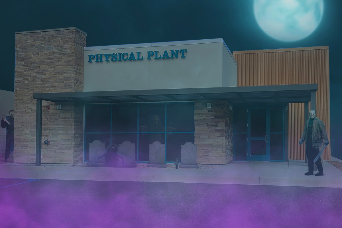 Exterior of the SJC Physical Plant on main campus with Michael Myers on the left peeking around the building, ghosts floating around and headstones by the front windows.