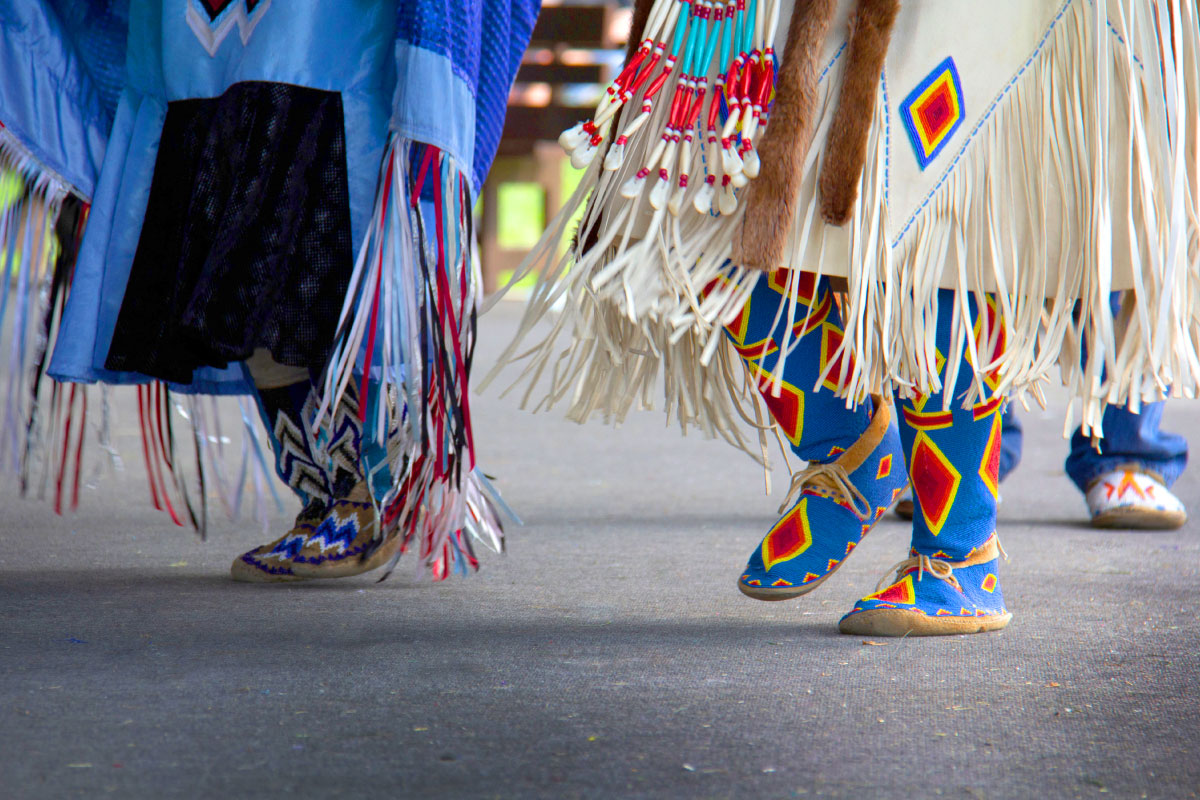 Two individuals in their traditional Native American moccasins dancing