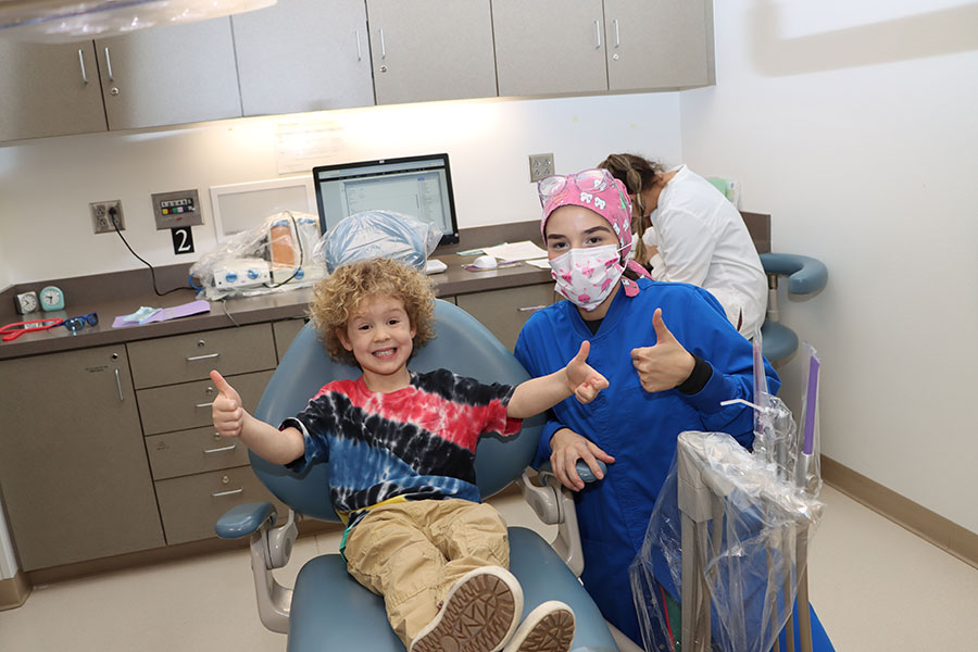 A kid sitting in a dental chair doing thumbs up with a hygienist to the right