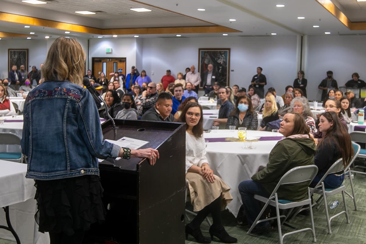 Person standing at podium speaking to a crowd of people.