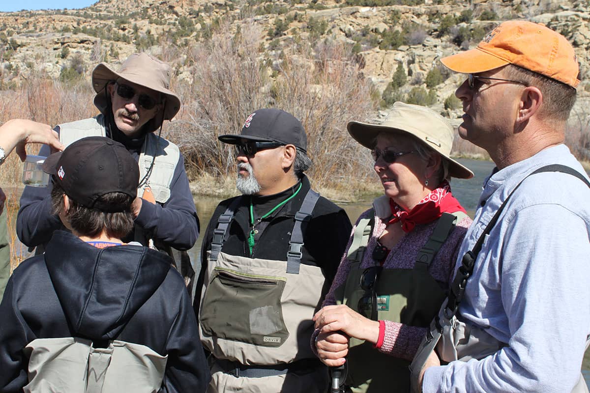 Group of people stand outside, getting instructions on fly fishing.