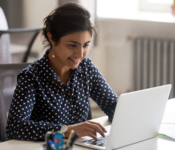 Person, wearing polka-dot blouse looking at laptop.