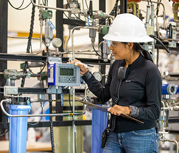 Person wearing white hardhat working on instrumentation controls.