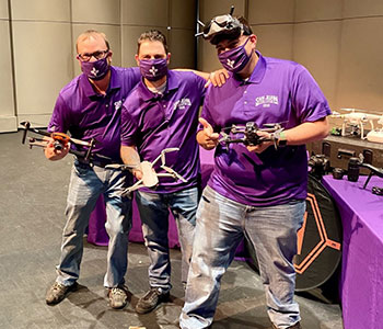 Three people holding drones.