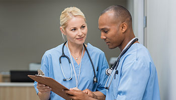 Two people wearing scrubs, looking over a medical chart.