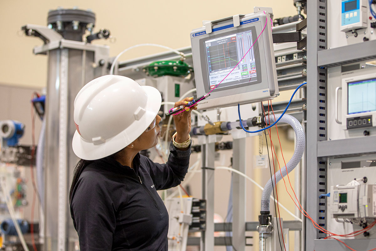 A person in a white hard hat looks at a monitor with various machines in the background