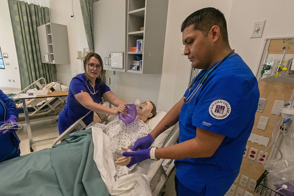 Two San Juan nursing students demonstrate checking a pulse and providing oxygen on a dummy