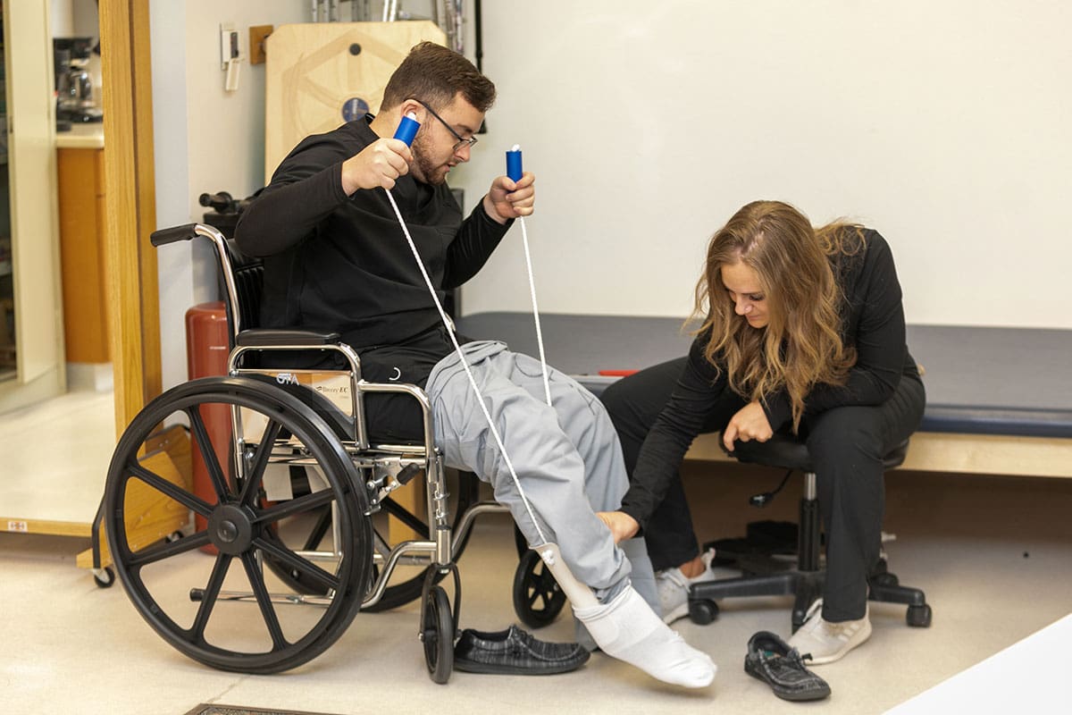 A student assesses the leg of another student who is sitting in a wheelchair