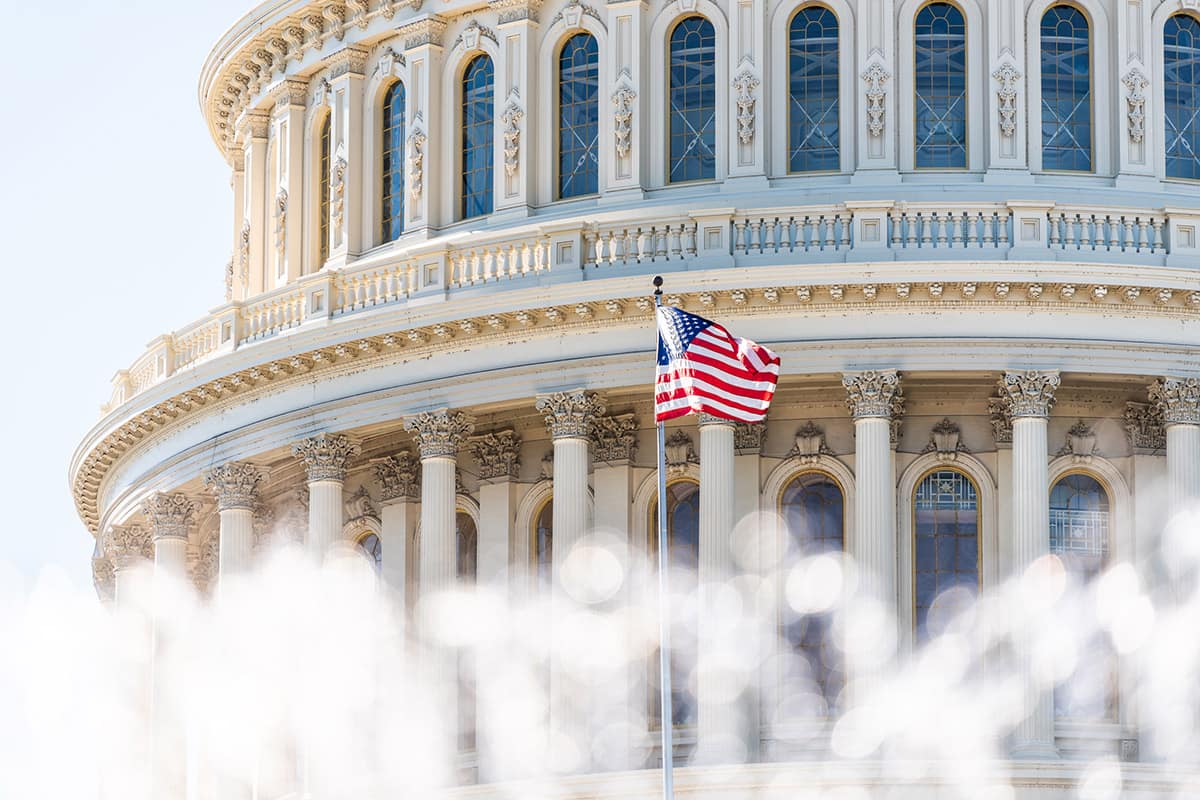 american flag waves in a breeze with the capitol building shown behind it.