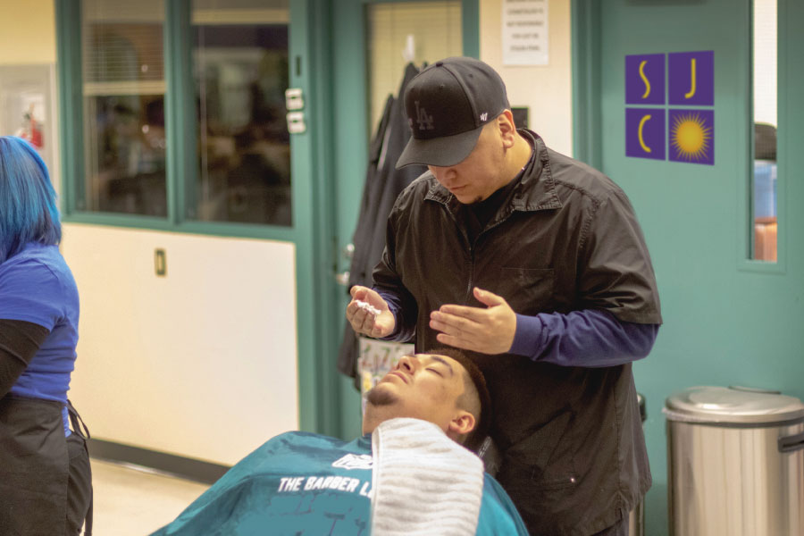 A San Juan College student preparing to put shaving cream on a man's face before a shave