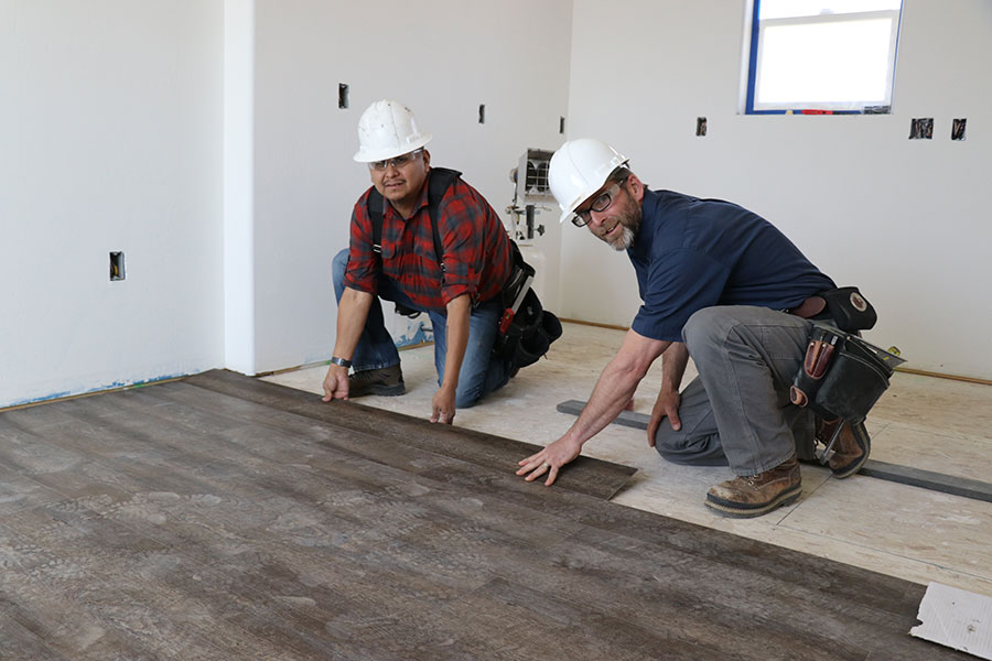 A San Juan College student with a professor laying flooring in a house.