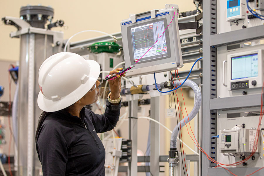 A person in a white hard hat looks at a monitor with various machines in the background