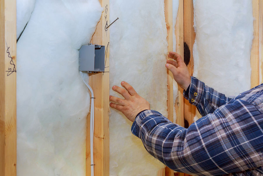 A man installing insulation into a framed wall.