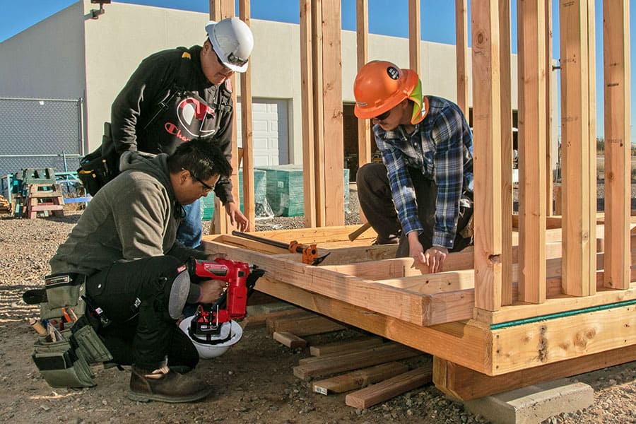 Two San Juan College students with a professor building the frame for a wall