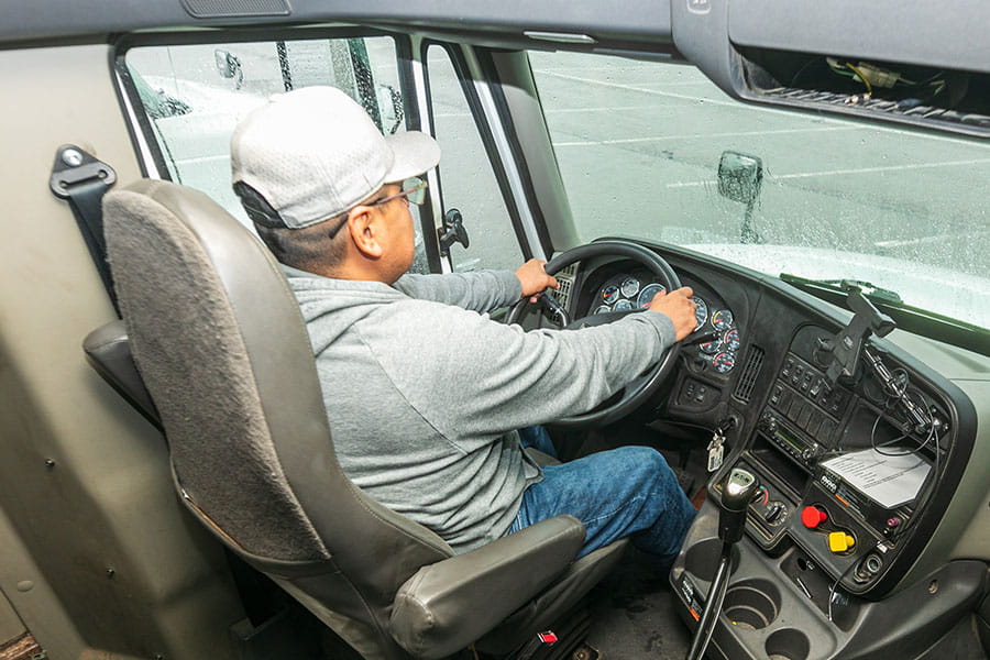 Individual sitting behind the steering wheel of a semi truck.