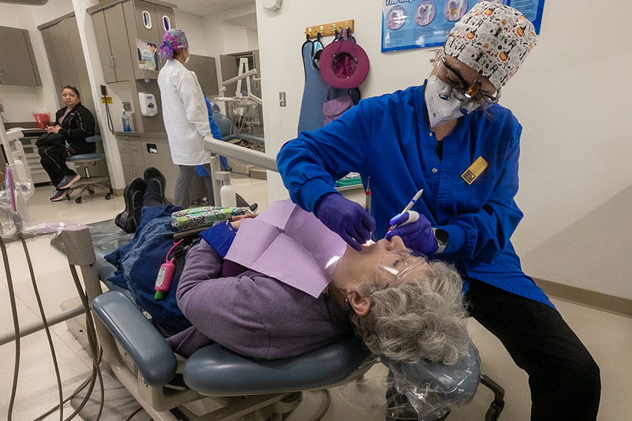 A student hygienist examines the mouth of a woman laying in a dental chair