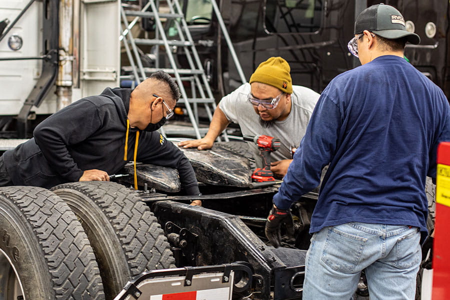 Three San Juan College students working on a diesel engine in a truck