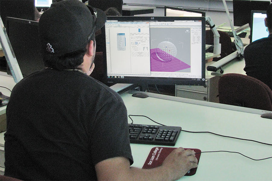 An individual wearing a black baseball hat sits in front of a computer monitor