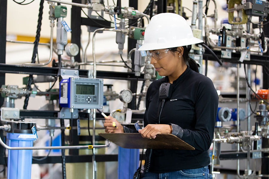 A person in a white hard hat looks at a monitor with various machines in the background