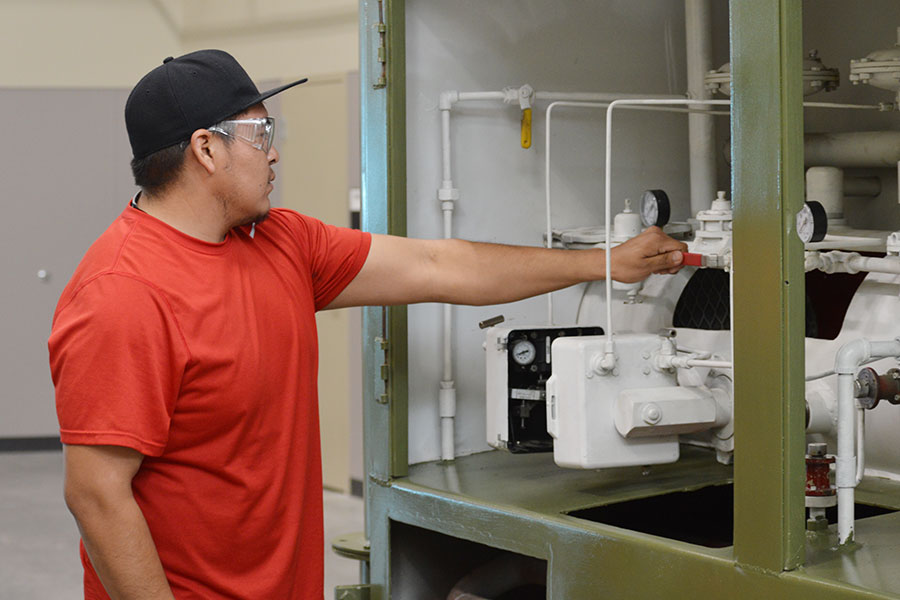 An individual wearing a hat and safety goggles turns the valve on production machinery