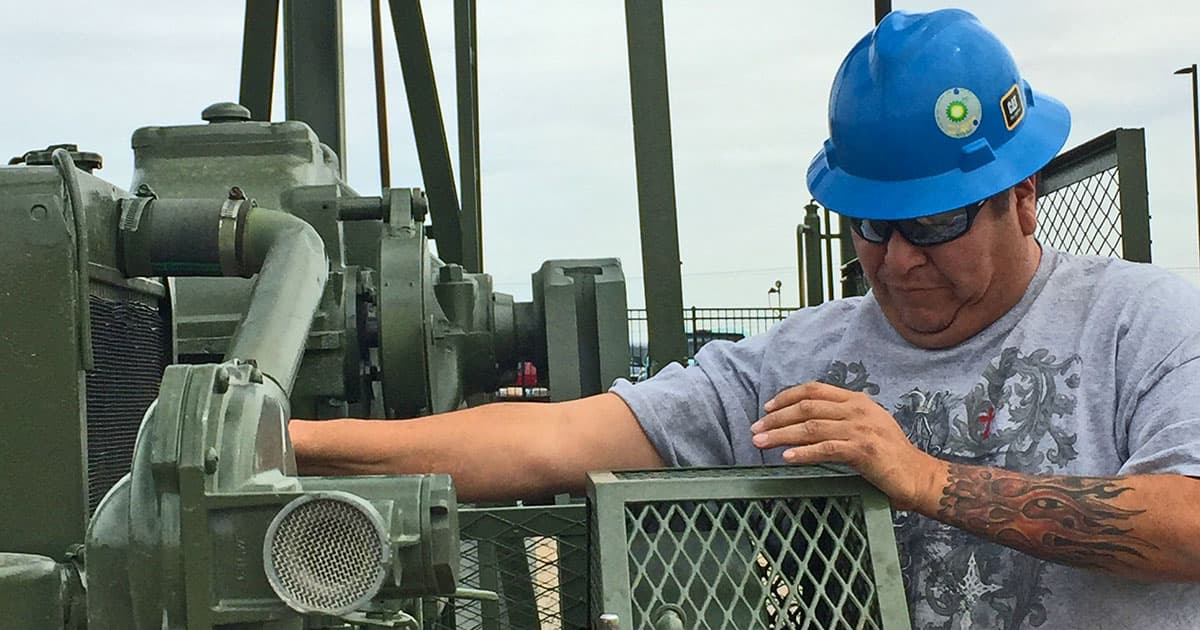 Man, wearing a blue hardhat, working on oil and gas equipment.