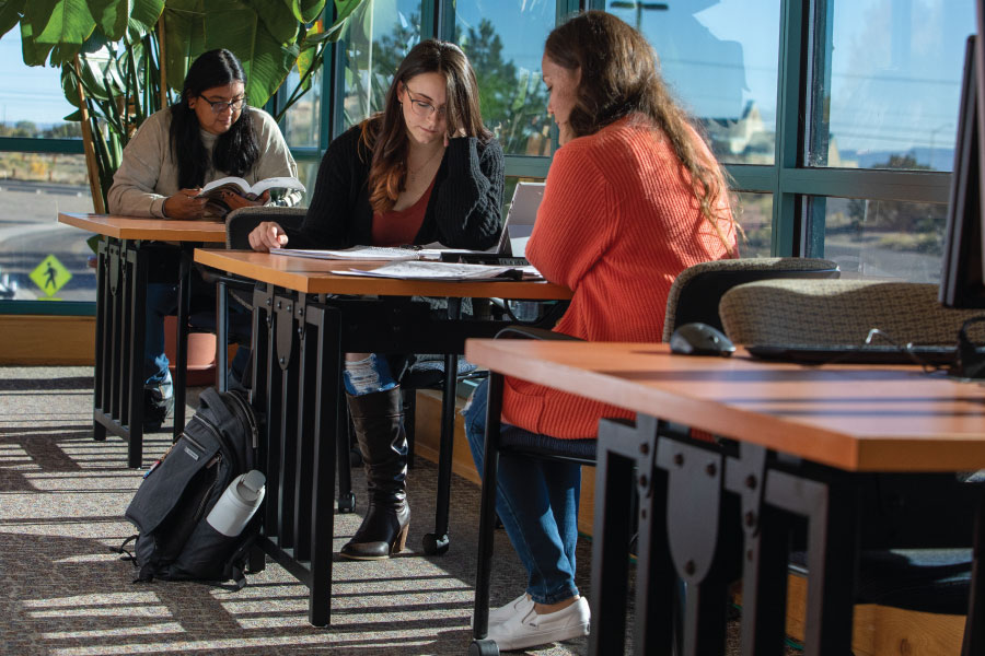 Tres estudiantes sentados en mesas en la biblioteca.