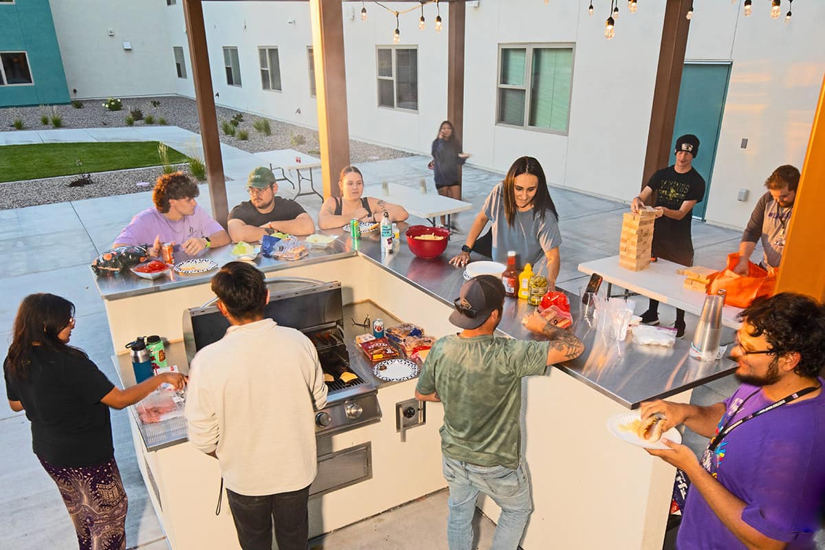 SJC students hang out around the outdoor BBQ grill on the patio at Student Housing enjoying games and food..