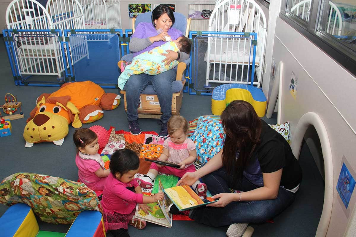 A CFDC teachers reading to three toddlers and one teacher feeding a baby