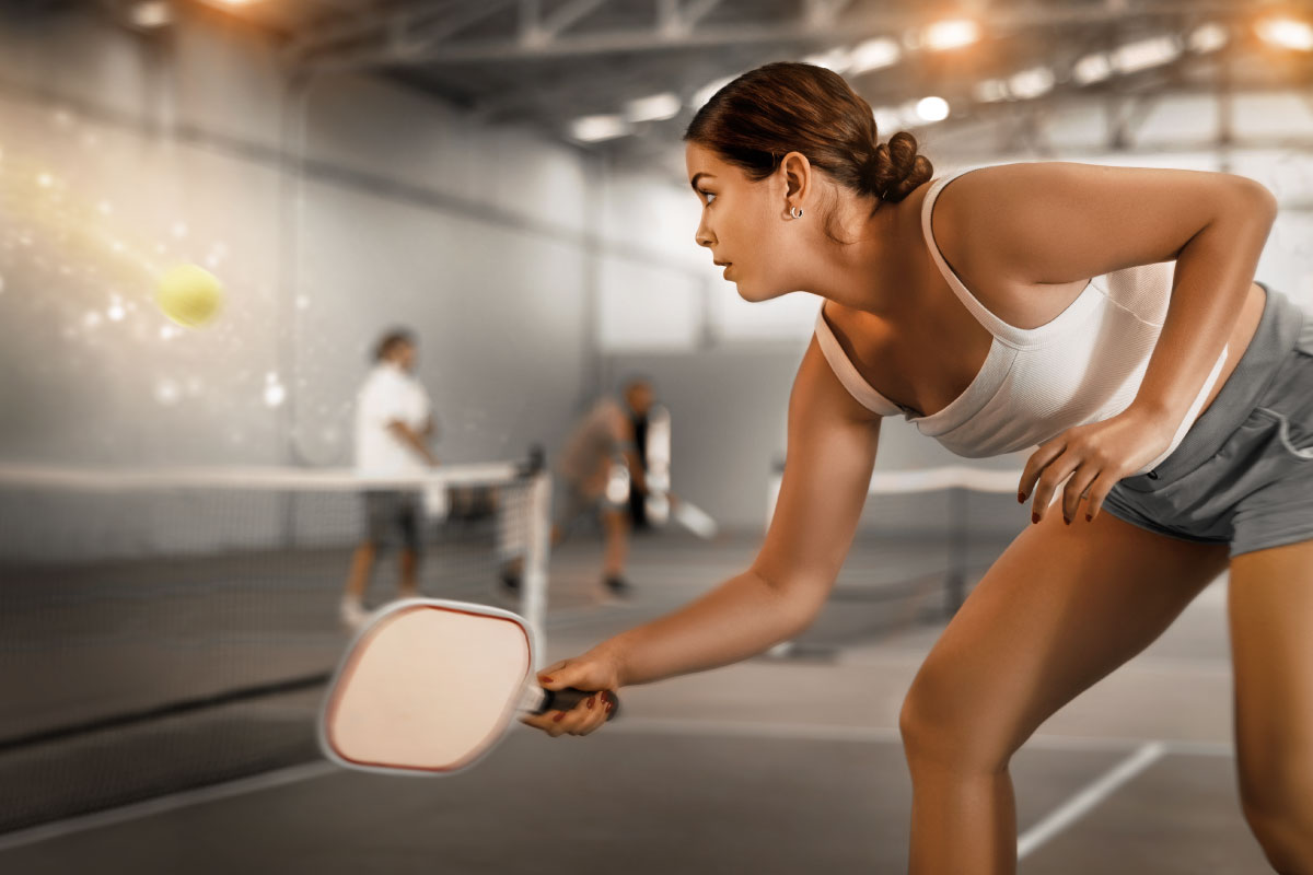 A women playing pickleball with a white paddle.