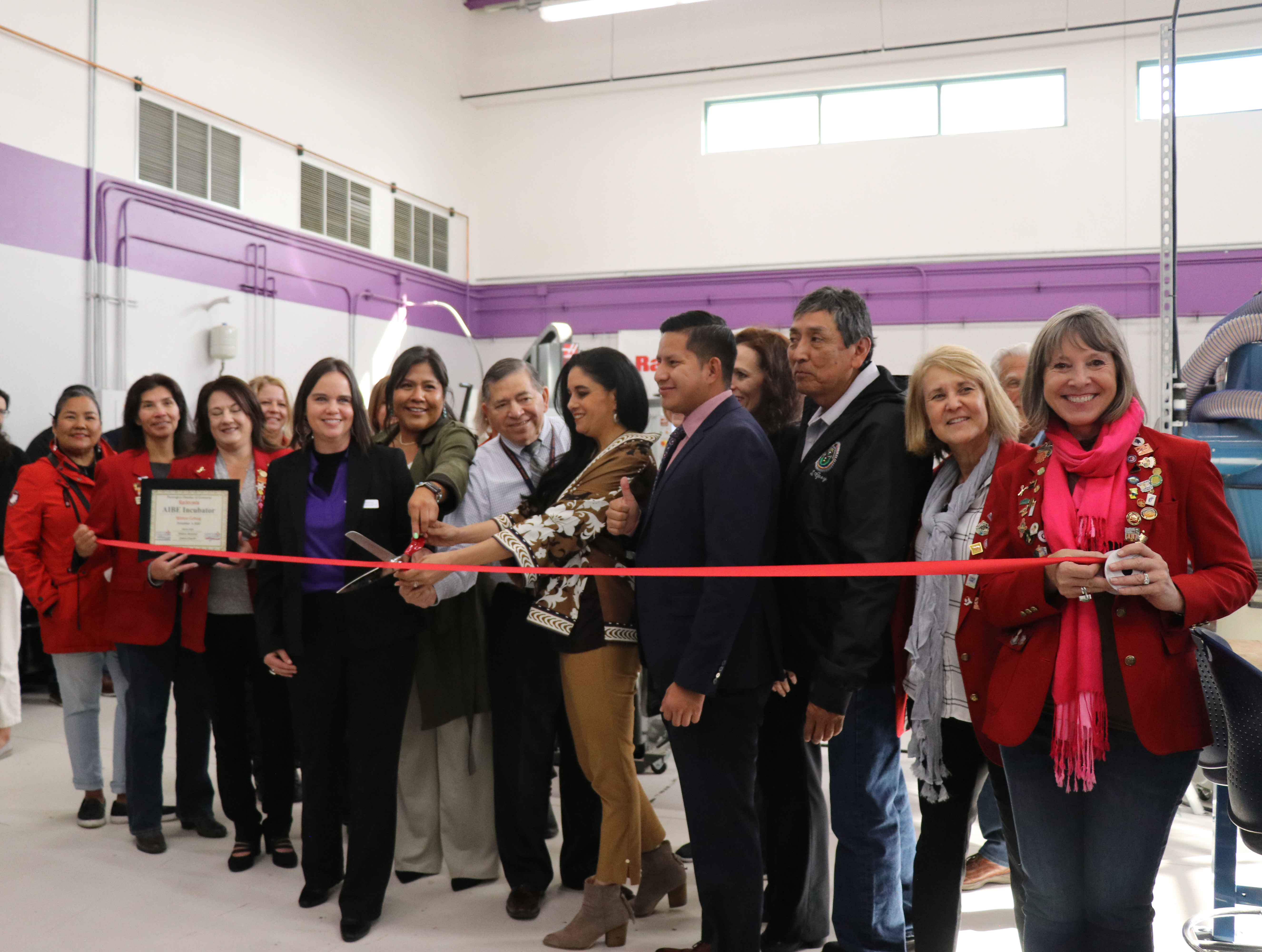 Group of people prepare for a red ribbon cutting.