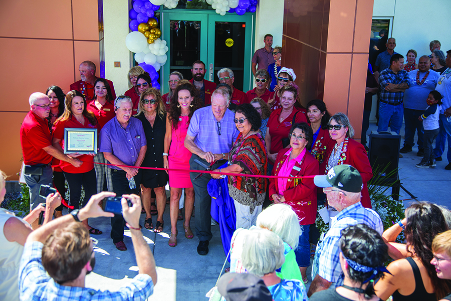 Group of people cutting a red ribbon in front of a new building